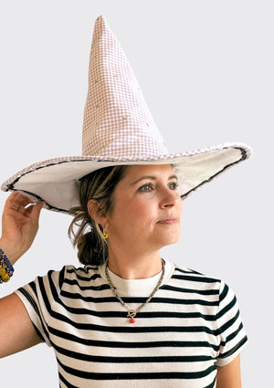 Person wearing a large checkered witch hat upcycled from a quilt against a plain background