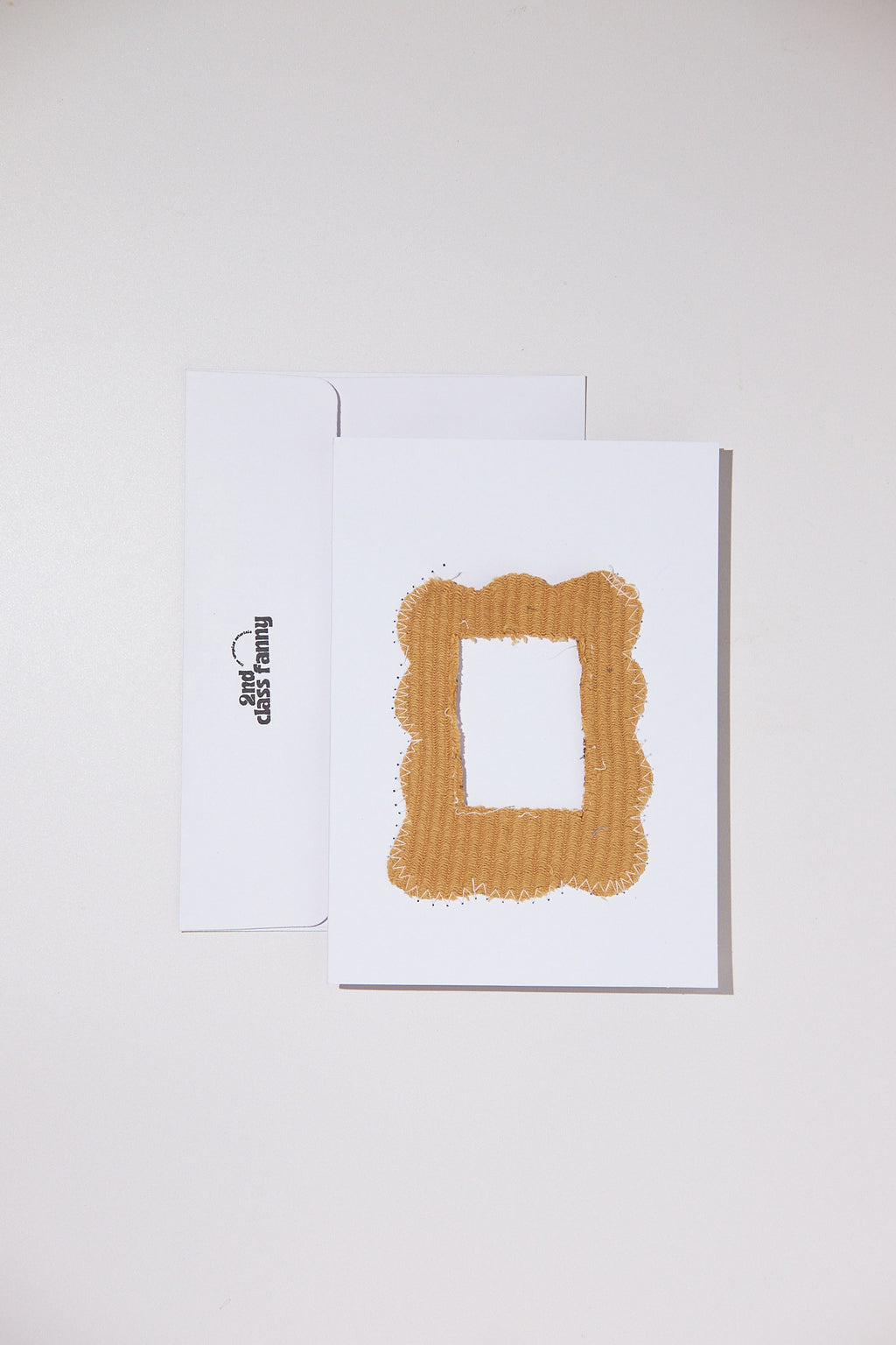 White card and envelope with a textured gold design made from fabric upcycled from a sweater, featuring an opening for your own Polaroid on a white background