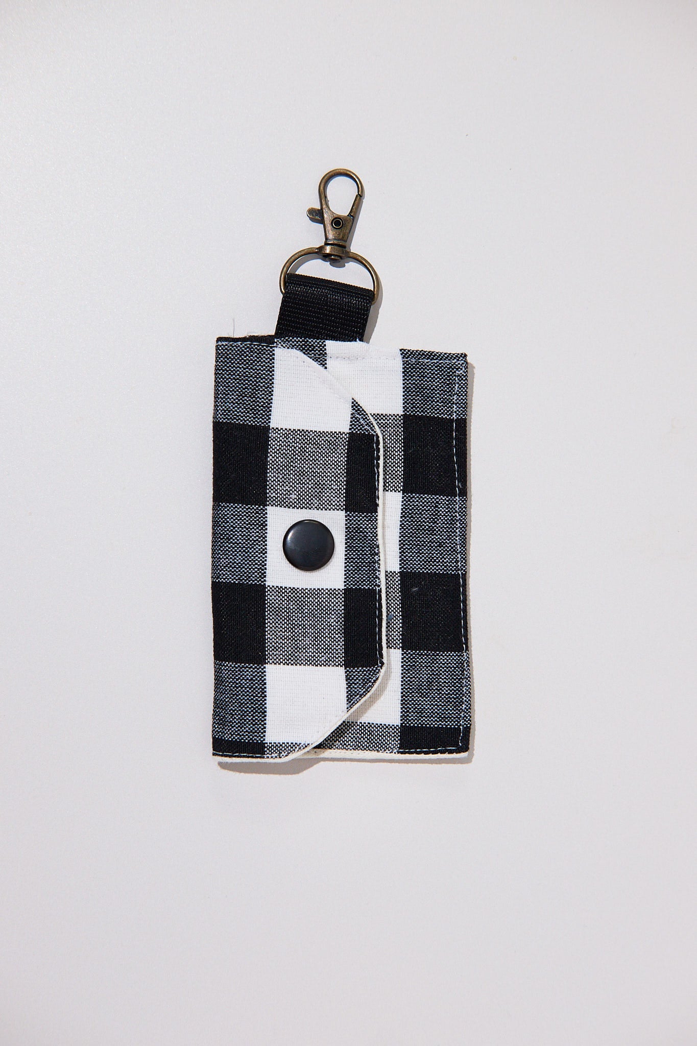 Black and white checkered keychain pouch with a black snap button  upcycled from curtains on a light gray background