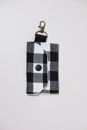 Black and white checkered keychain pouch with a black snap button  upcycled from curtains on a light gray background