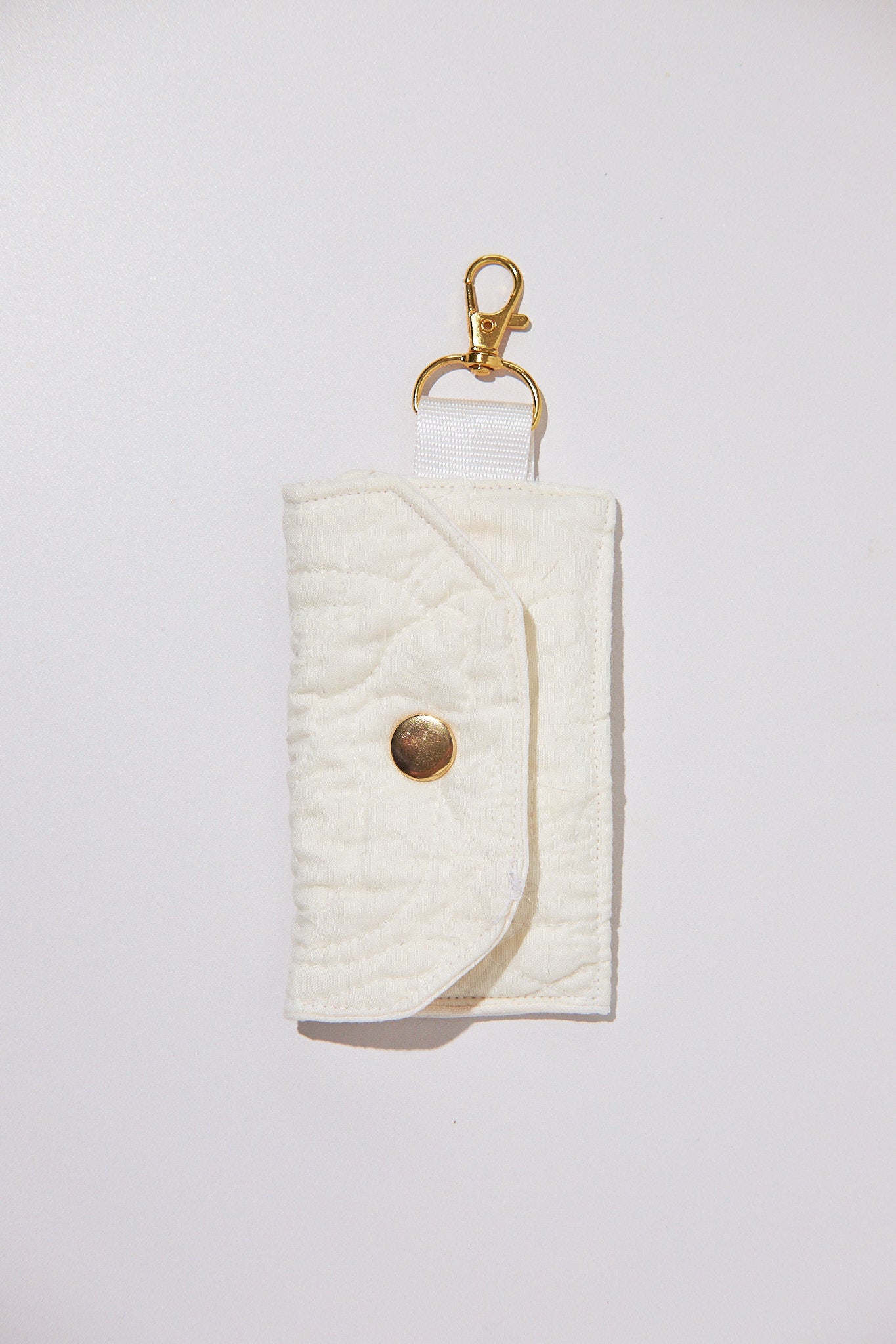 White quilted cardholder with a gold button and keychain upcycled from a quilt, on a light gray background
