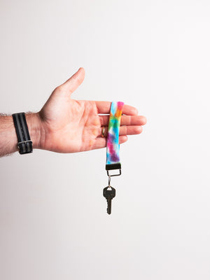 Hand holding a key with a tie dye  keychain upcycled from a shirt against a white background