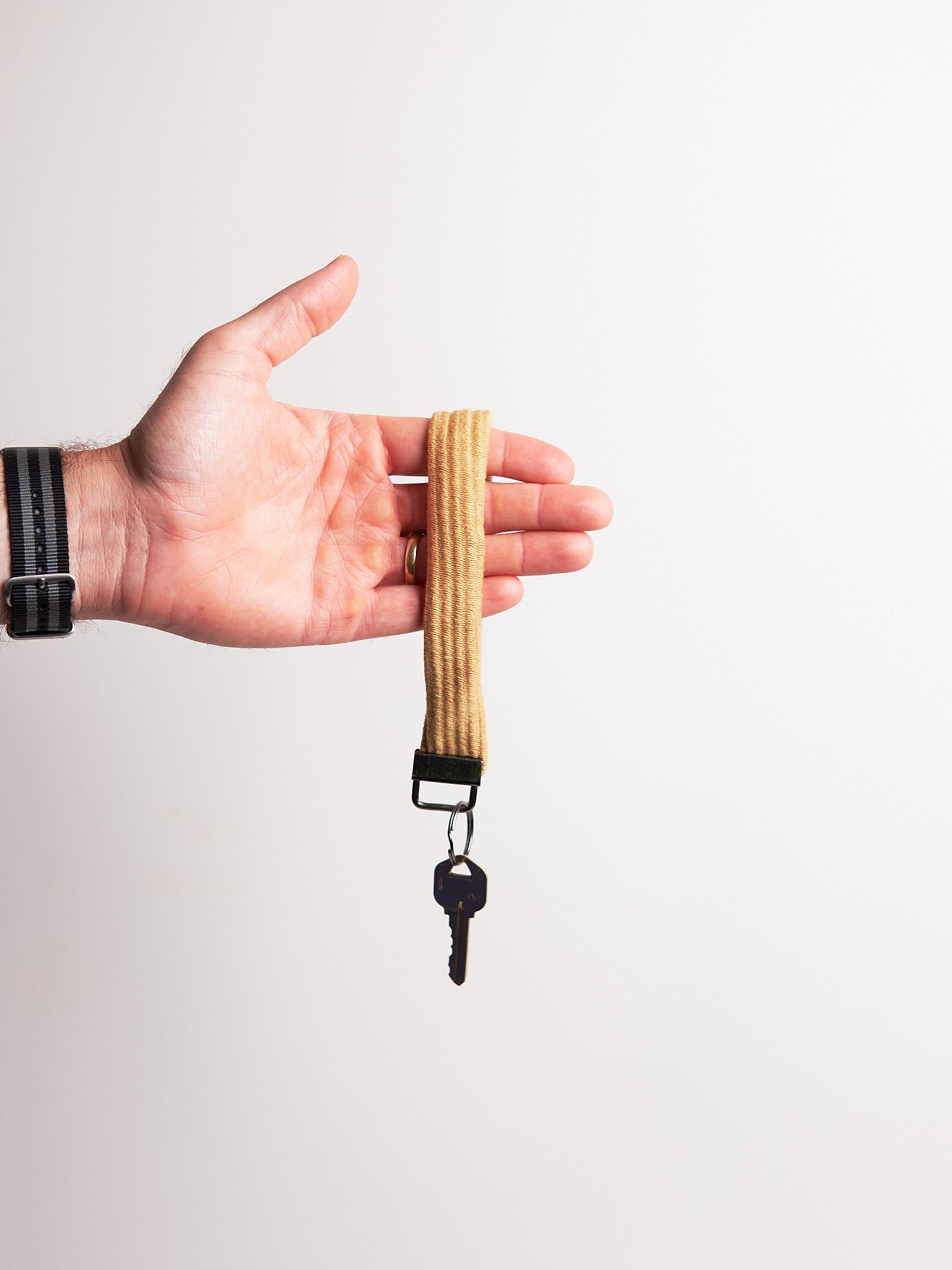 Hand holding a key chain upcycled from a sweater with a key attached on a light gray background