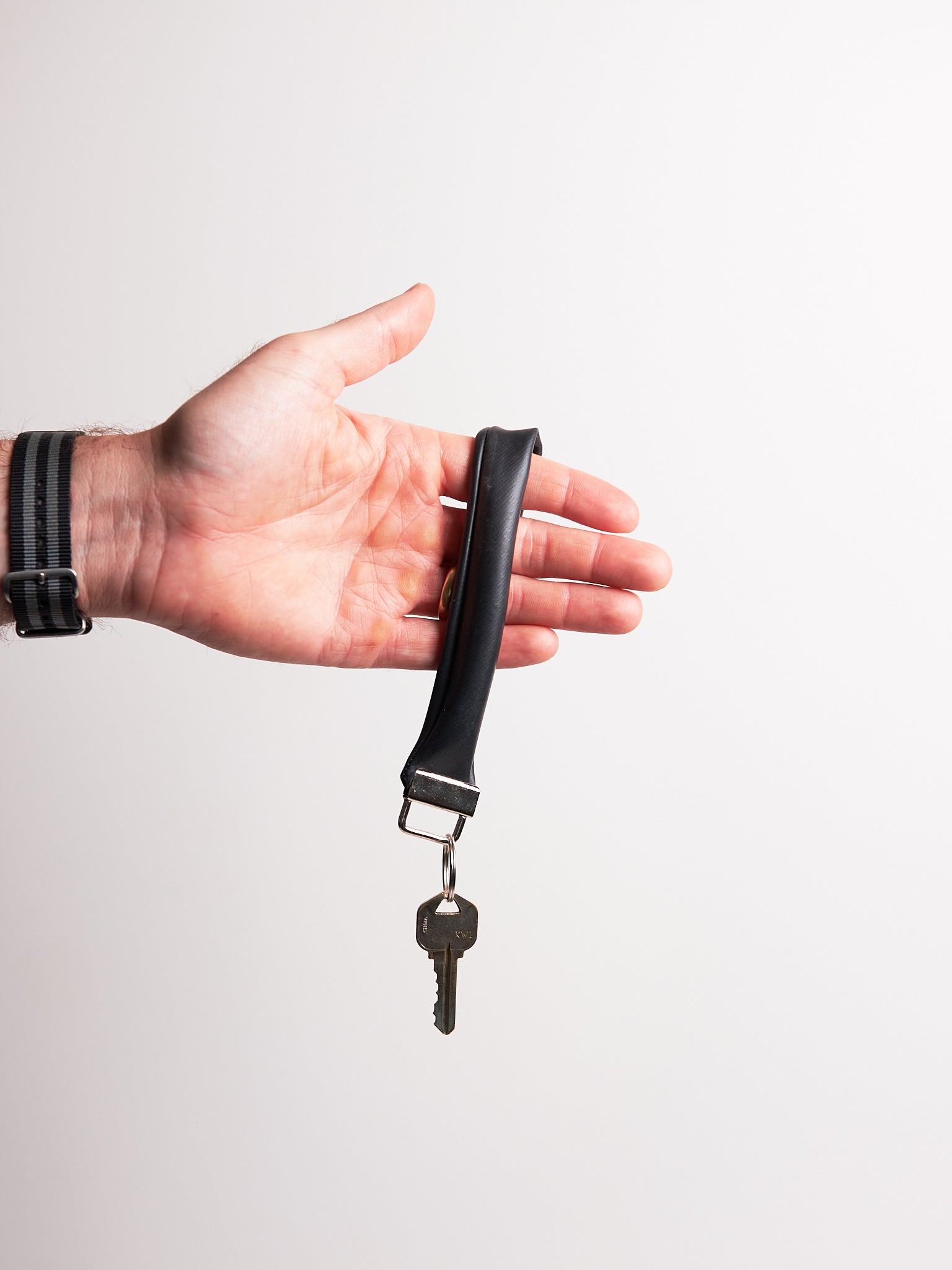 Hand holding a black keychain with a key upcycled from an inner tube against a light gray background