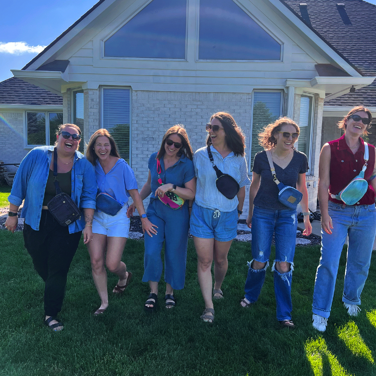Group of six women posing together in front of a house with shoulder bags