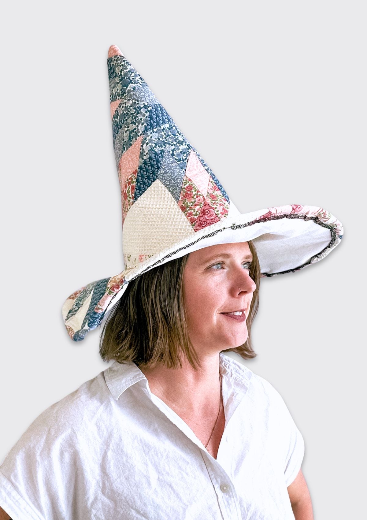 Woman wearing a colorful witch hat upcycled from a quilt against a white background