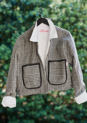 Houndstooth jacket with large pockets on a hanger upcycled from deadstock upholstry fabric against a green leafy background