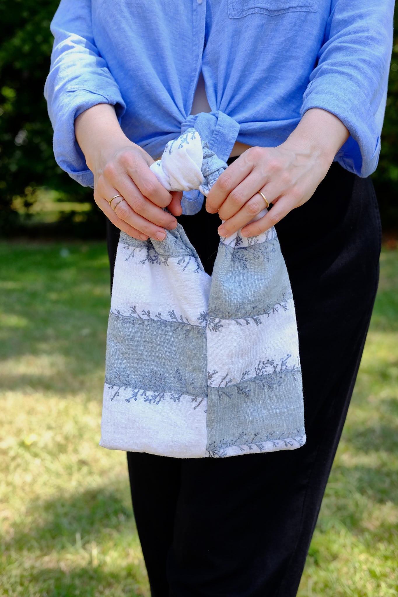 Person holding a white and blue knot bag coral patterns, upcycled form designer deadstock fabric outdoors