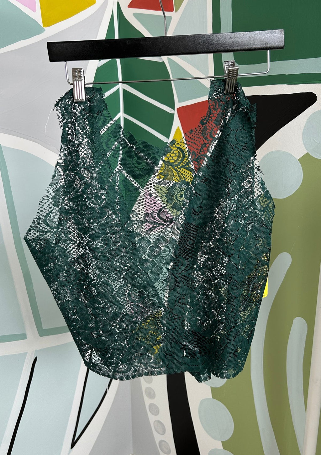 Green lace top on a hanger against a colorful abstract background
