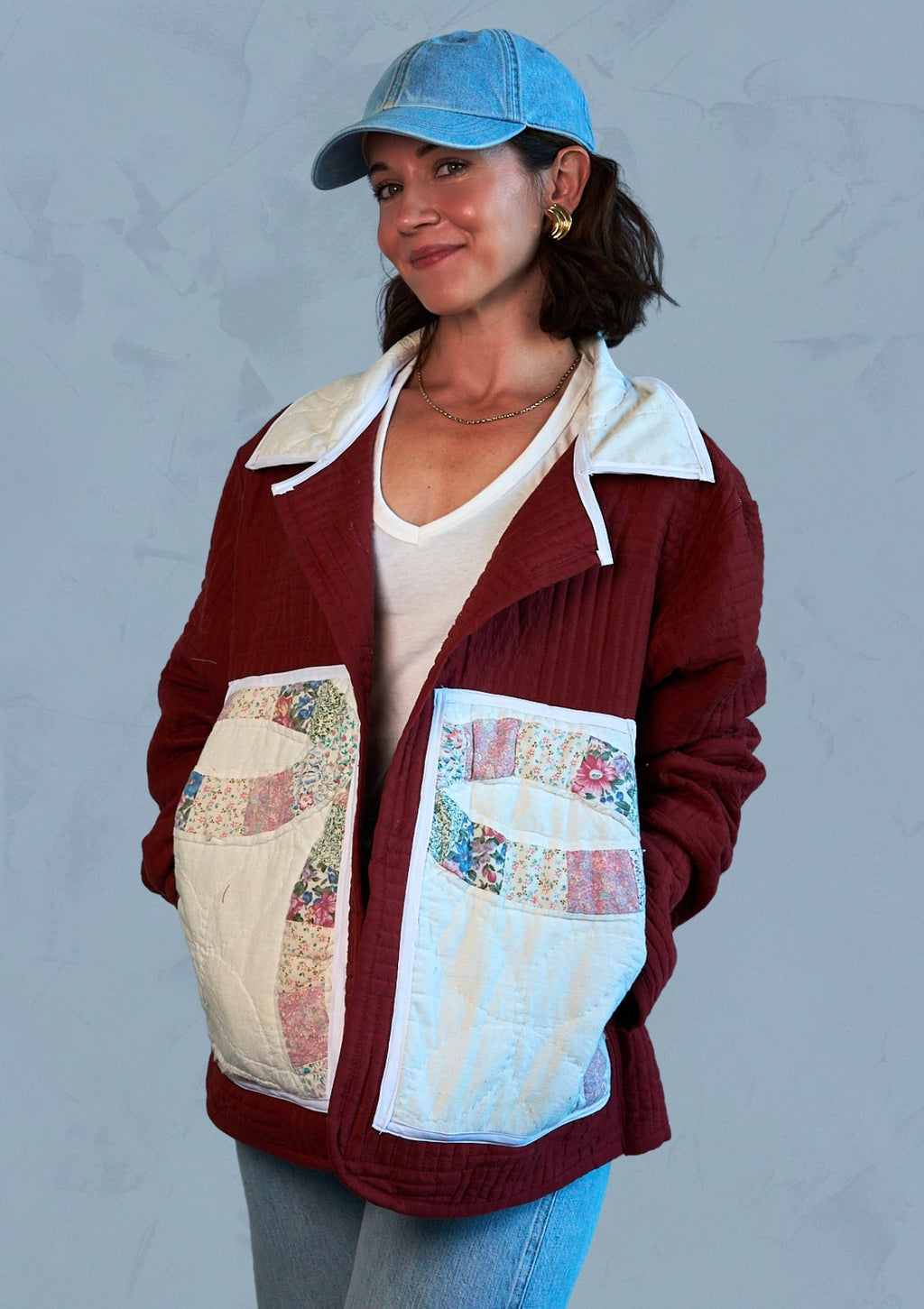 Woman wearing a maroon jacket with patchwork pockets upcycled from a quilt against a gray background