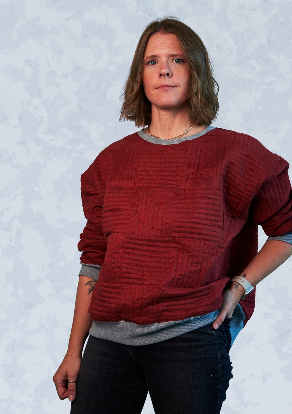 Person wearing a red textured crew neck sweatshirt upcycled from comforter against a light gray background