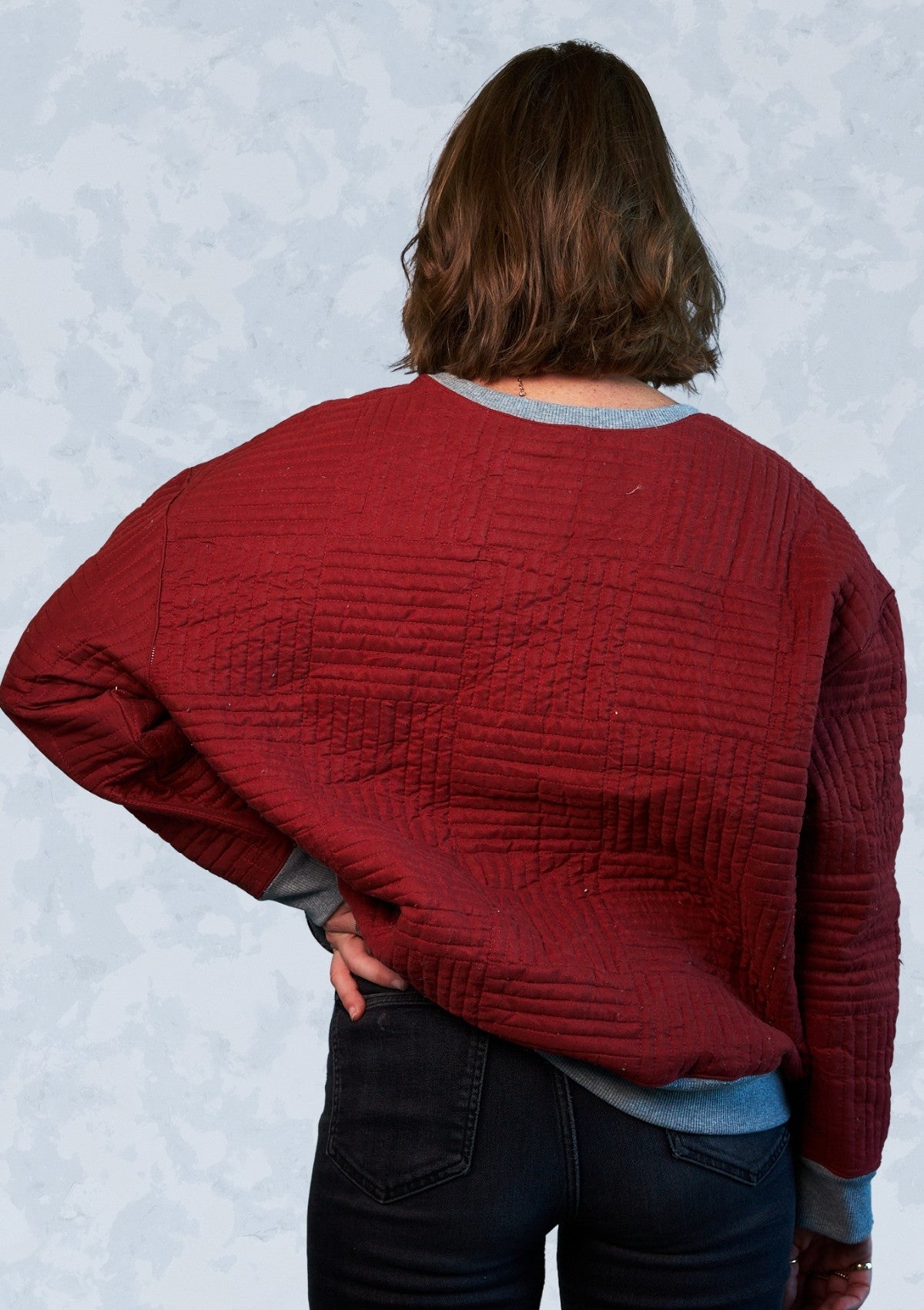 Person wearing a red textured crew neck sweatshirt upcycled from a comforter with a light gray background