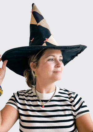 Person wearing a black and beige witch hat upcycled from a quilt against a white background