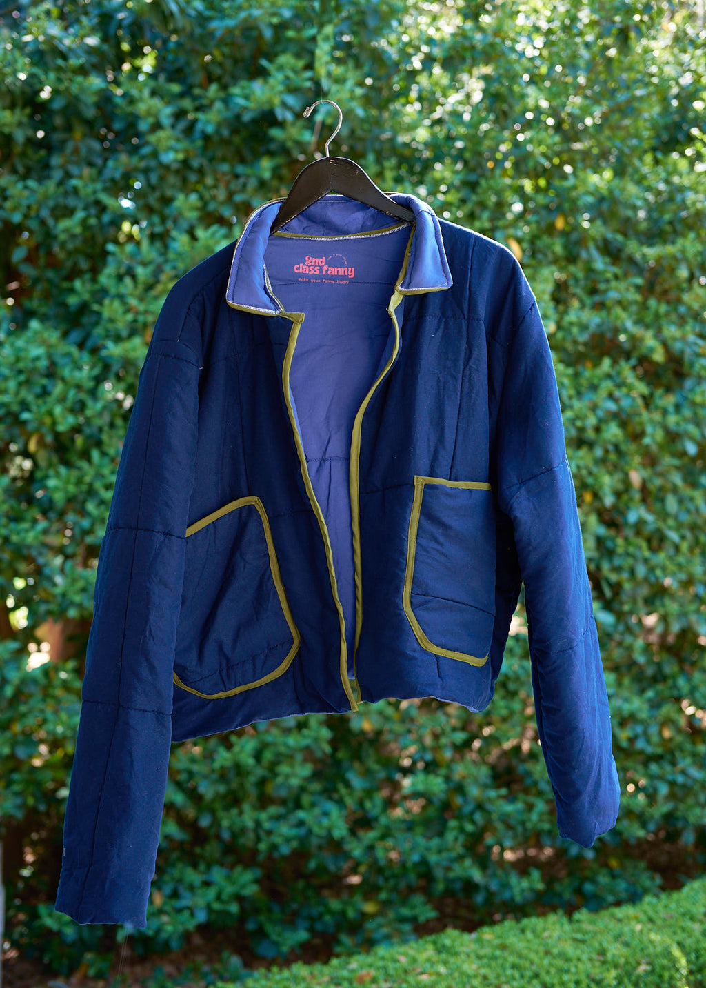Blue jacket with yellow accents on a hanger against a green bush background