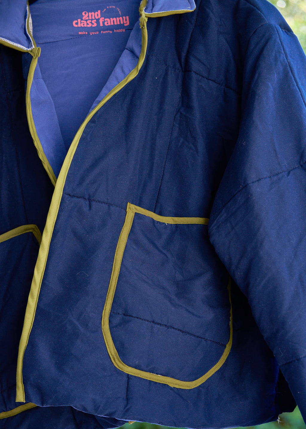 Navy blue jacket with green accents and a visible brand logo on a blurred natural background