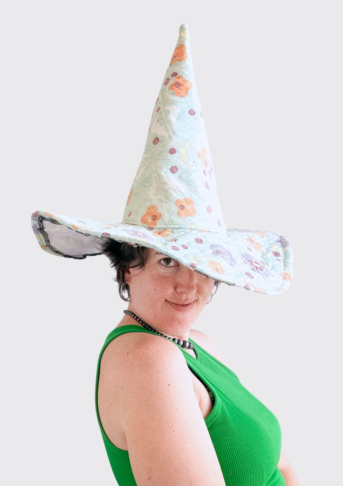 Person wearing a cone-shaped witches hat with floral pattern upcycled from a quilt on a plain background