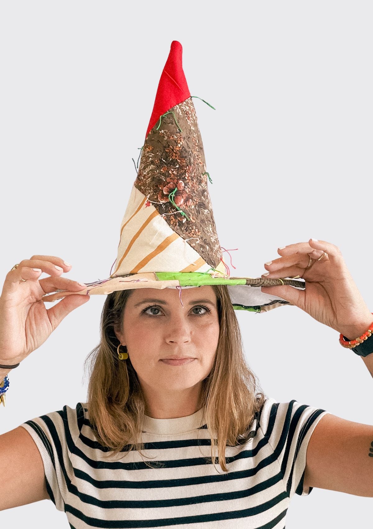 Person wearing a patchwork pattern witches hat with a red top and various designs upcycled from a quilt on a white background