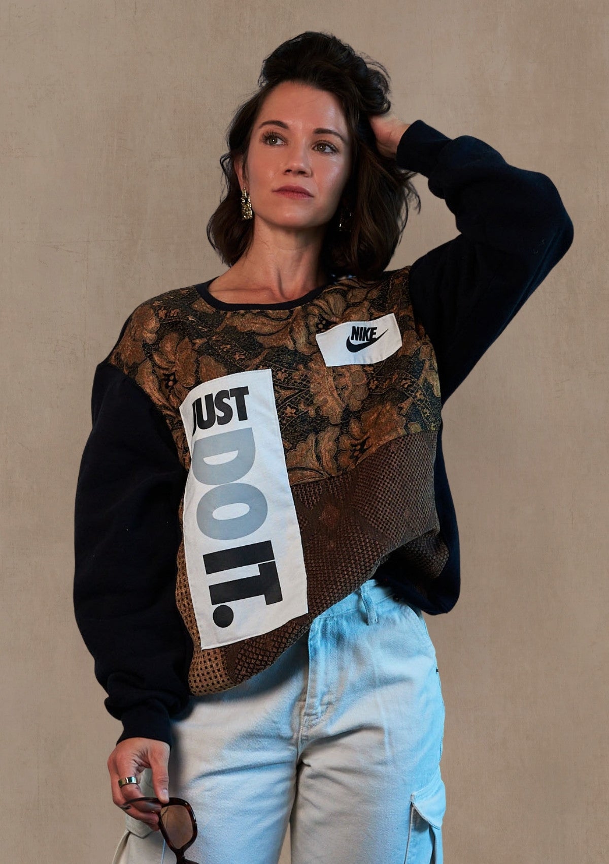 Person wearing a Nike sweatshirt with 'Just Do It.' design upcycled from a crew neck, curtains, and a Nike tank, against a beige background