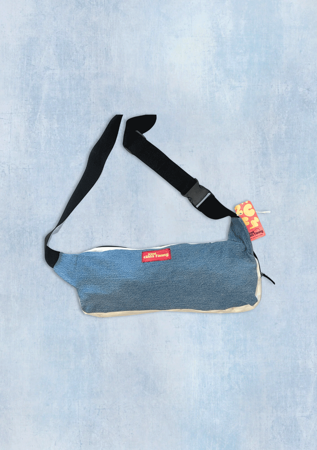Blue denim bag with a black strap on a light blue textured background