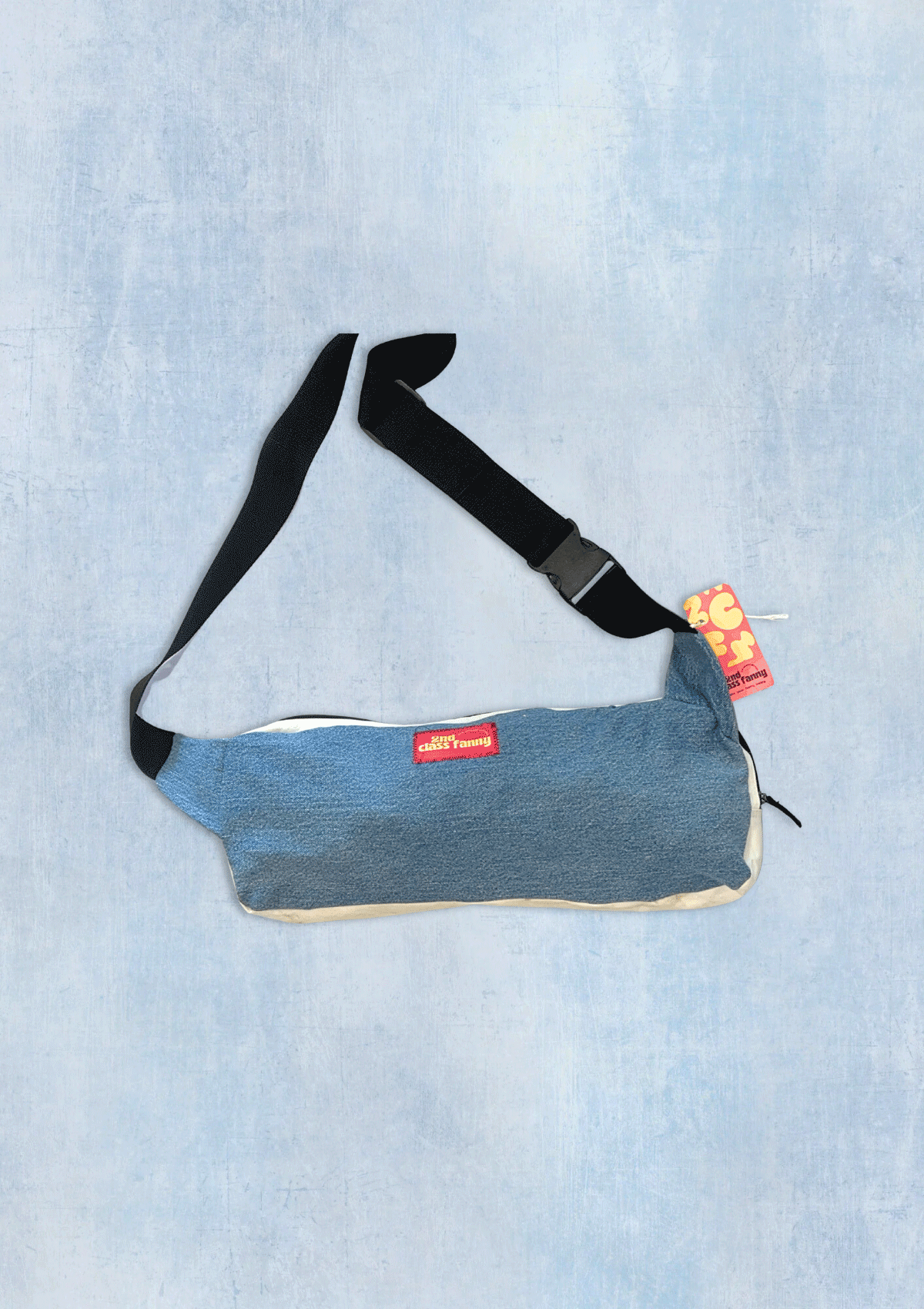 Blue denim bag with a black strap on a light blue textured background