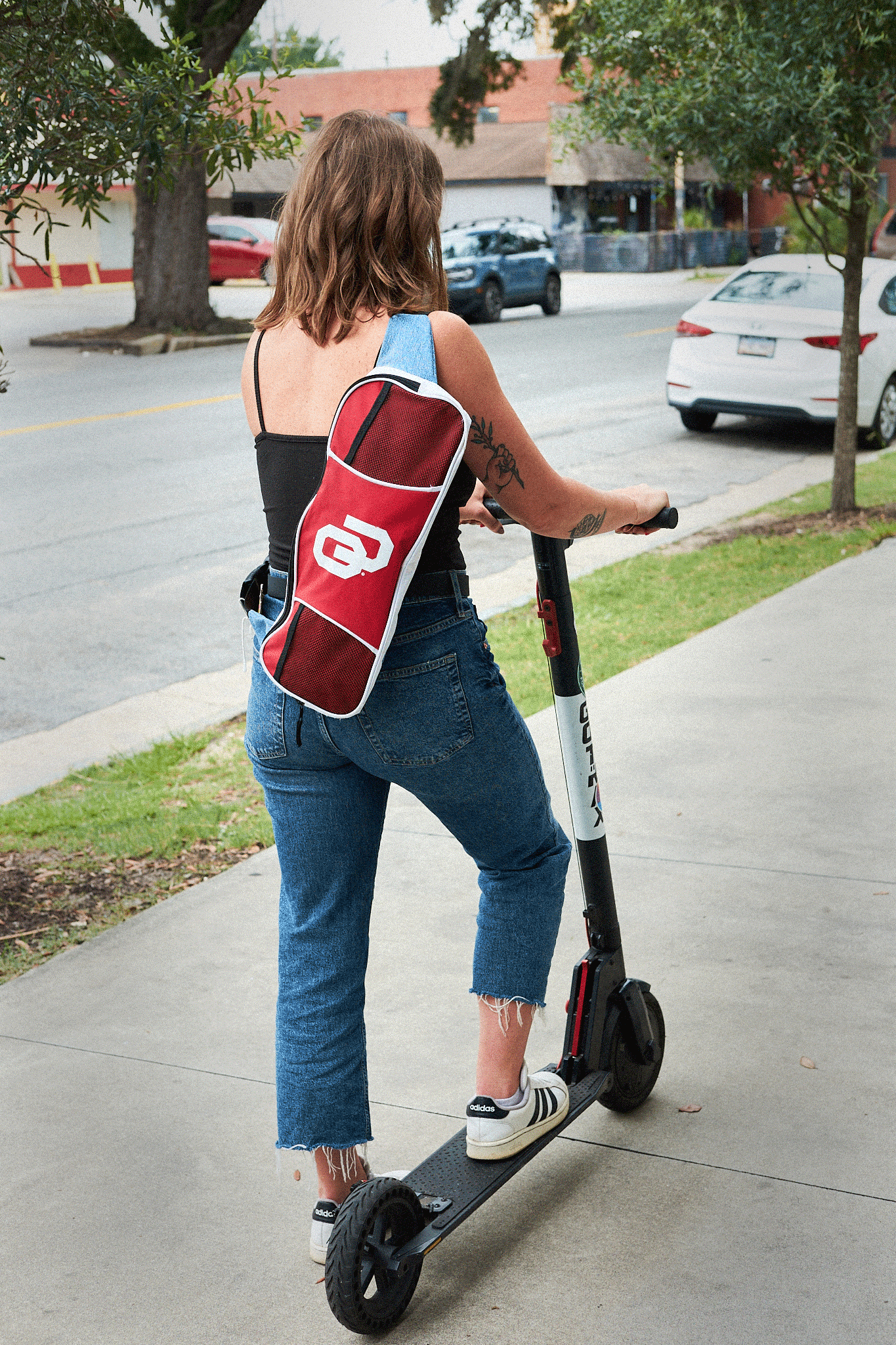 Woman riding a scooter with a red OU bike bag on a sidewalk