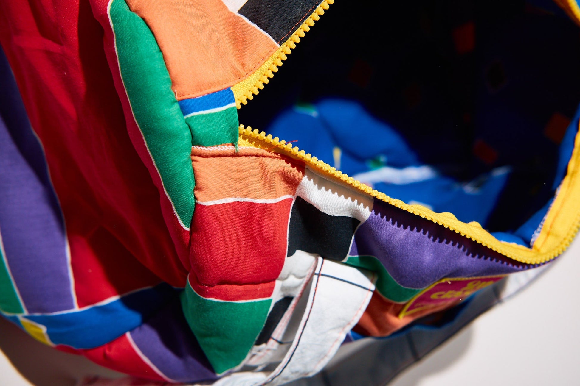 Close-up of a colorful quilt with a zipper, featuring red, green, blue, and purple patterns upcycled from comforter.