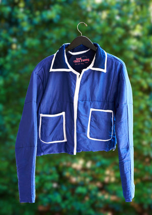 Blue jacket with white accents on a hanger against a green leafy background