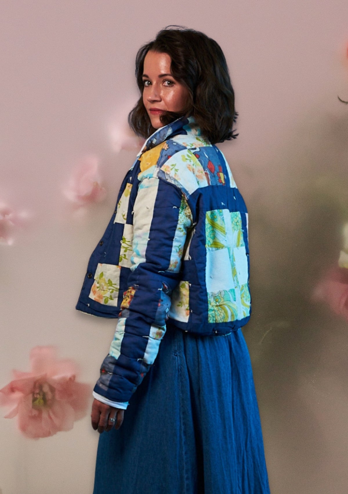 Person wearing a colorful patchwork jacket upcycled from a quilt with a plain background