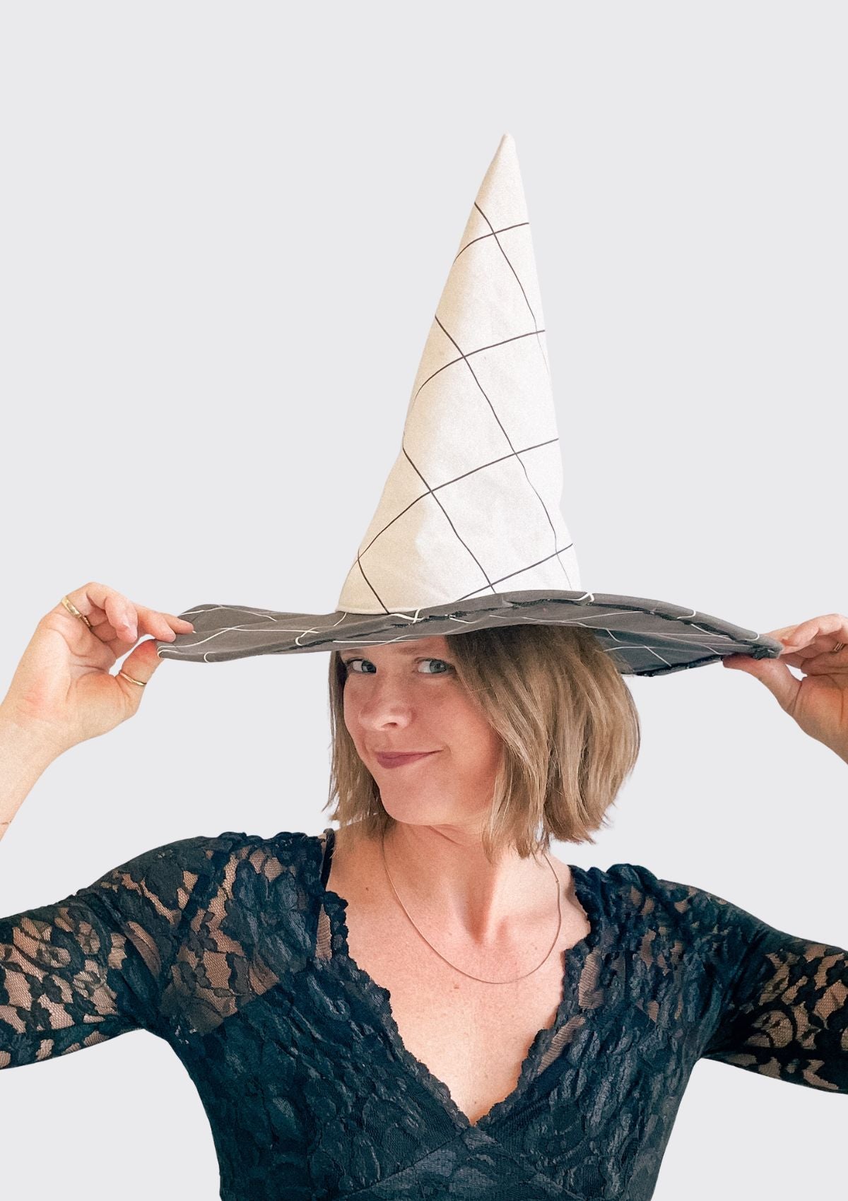 Person wearing a large witch hat with a geometric pattern upcycled from a duvet on a plain background