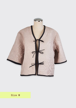 Beige quilted jacket with black trim and tie front closure upcycled from comforter on a mannequin against a light gray background