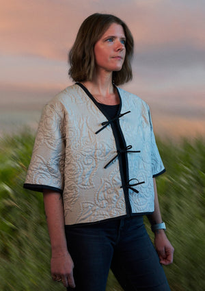 Woman wearing a patterned tie front jacket upcycled from comforter standing in a field with a blurred background
