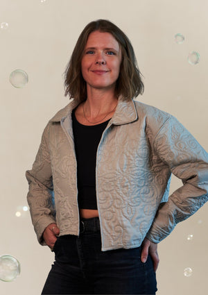Woman wearing a textured beige jacket upcycled from comforter, standing against a neutral background.