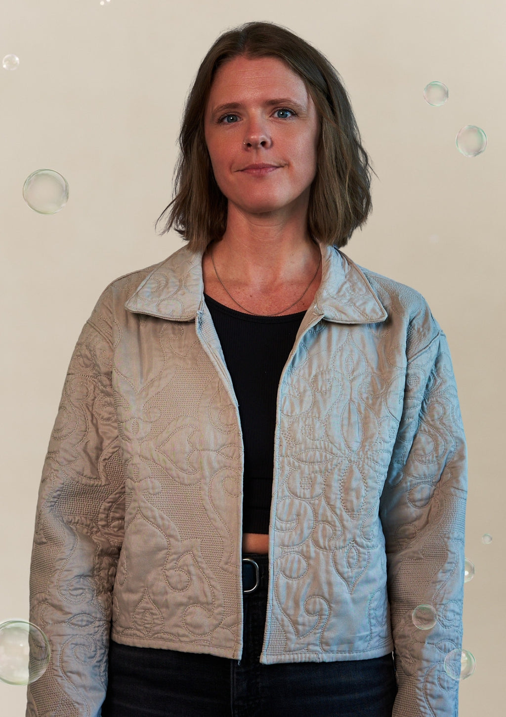 Woman wearing a textured beige jacket upcycled from a comforter over a black top with a plain background