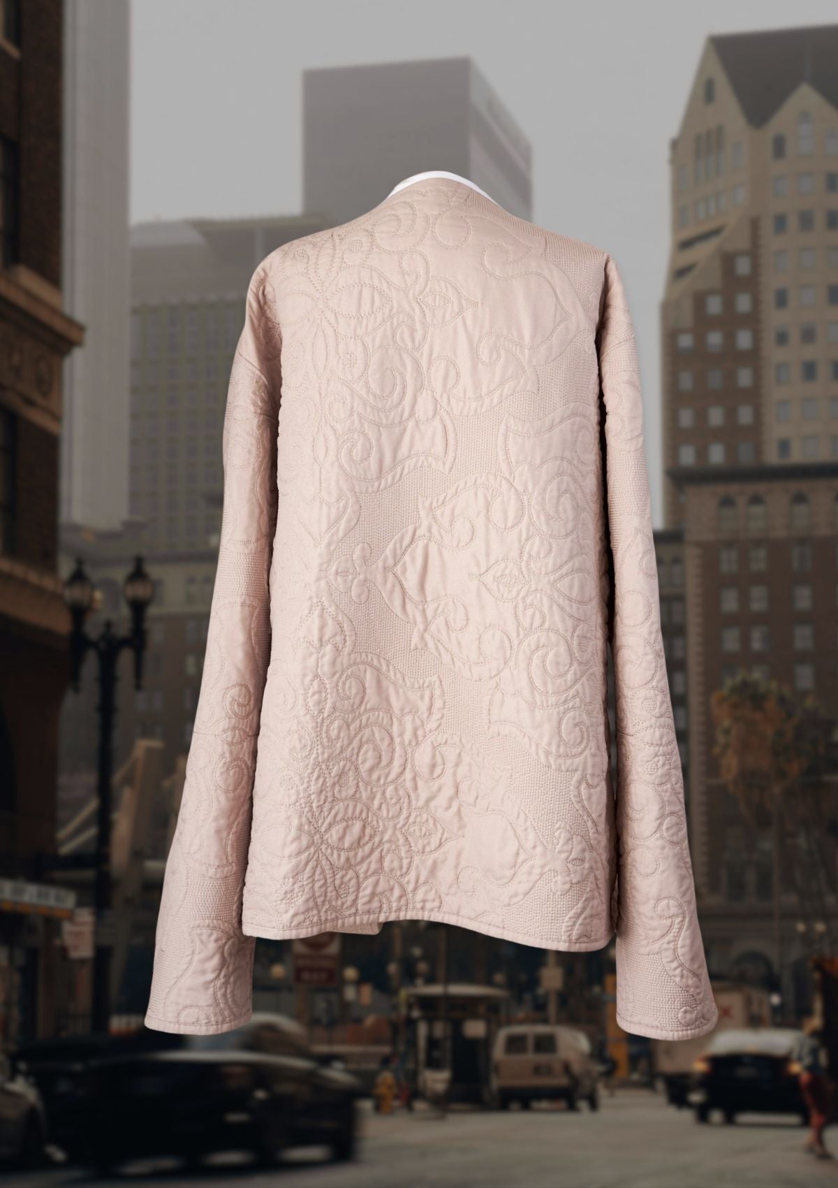 Back of a beige textured coat on a mannequin with a cityscape background