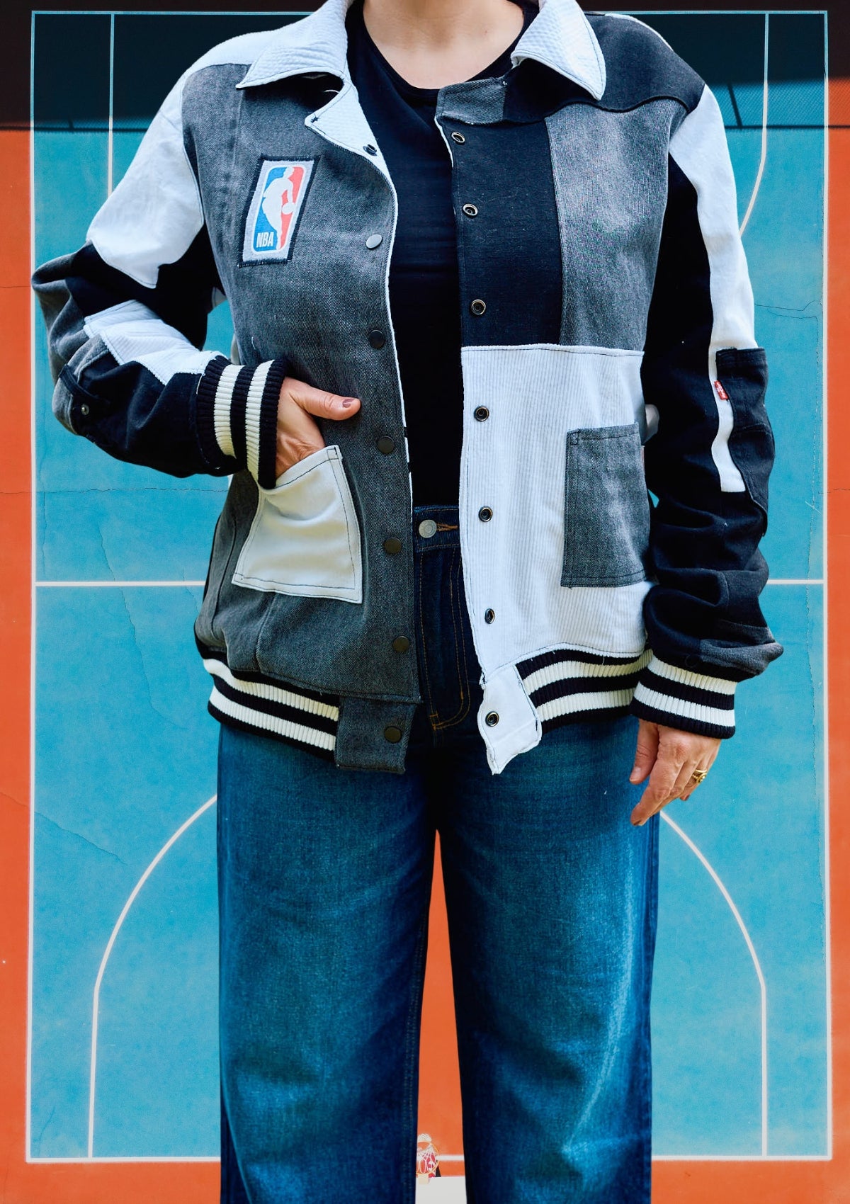 Person wearing a black, white, and gray Varsity style jacket, upcycled from denim for NBA Spurs Basketball, with a logo on a colorful background