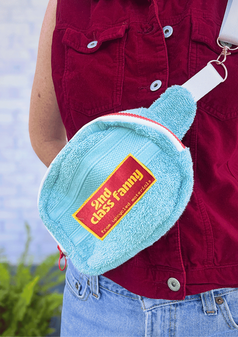 Light blue fanny pack upcycled from a towel with pink label reads 2nd Class Fanny worn by a person in a red jacket.