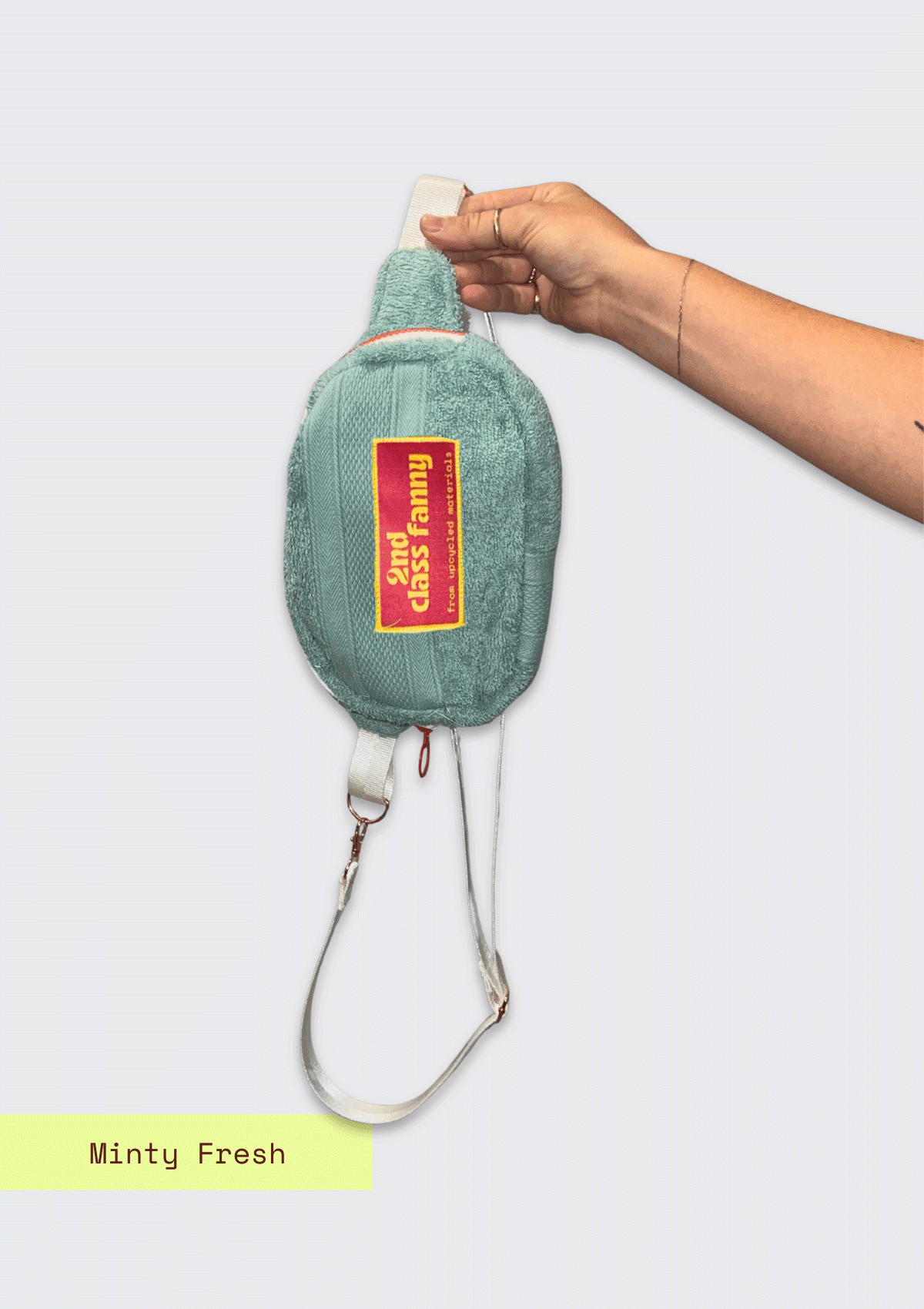 Fanny pack upcycled from a towel with a pink label held by a hand on a white background