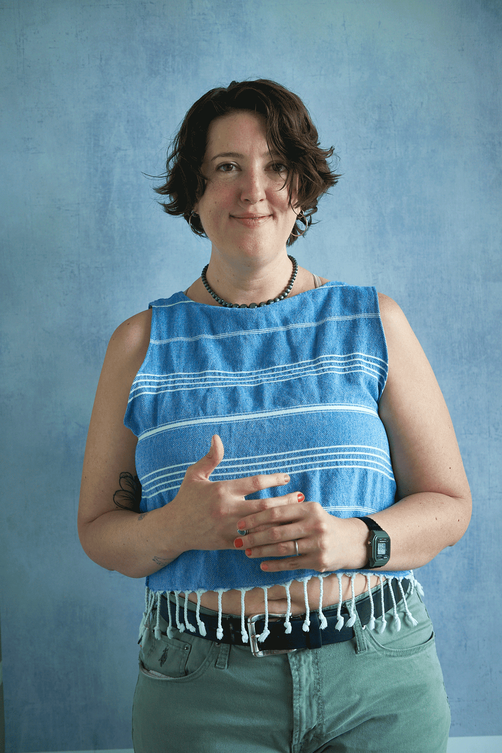Woman wearing a blue sleeveless top with white fringe upcycled from a turkish towel against a blue background