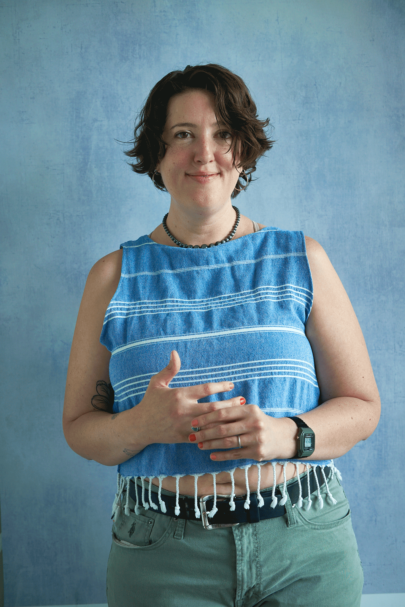 Woman wearing a blue sleeveless top with white fringe upcycled from a turkish towel against a blue background