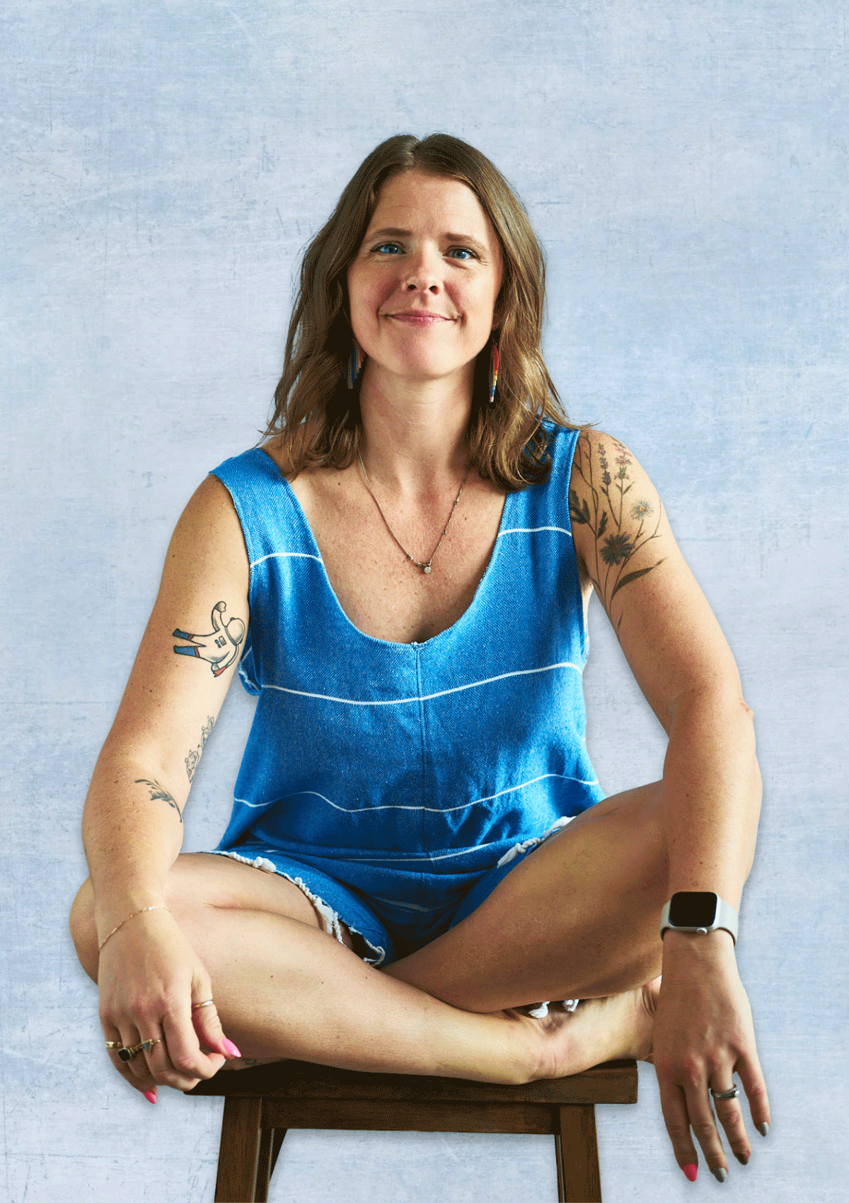 Woman wearing a blue sleeveless romper sitting on a chair against a light blue background