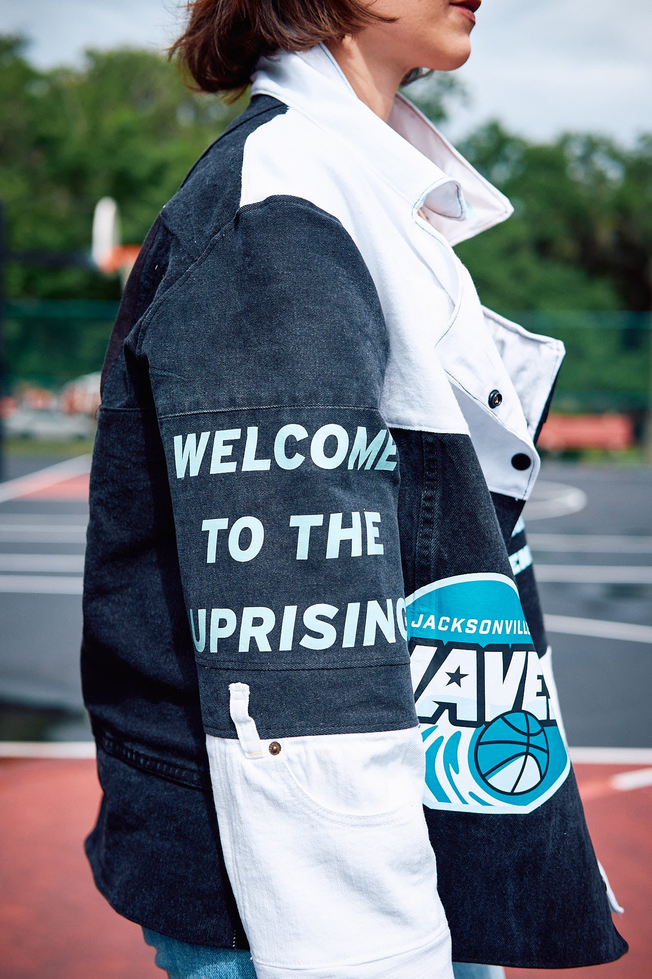 Person wearing a jacket with 'Welcome to the Uprising Jacksonville Waves' text on a sports court background