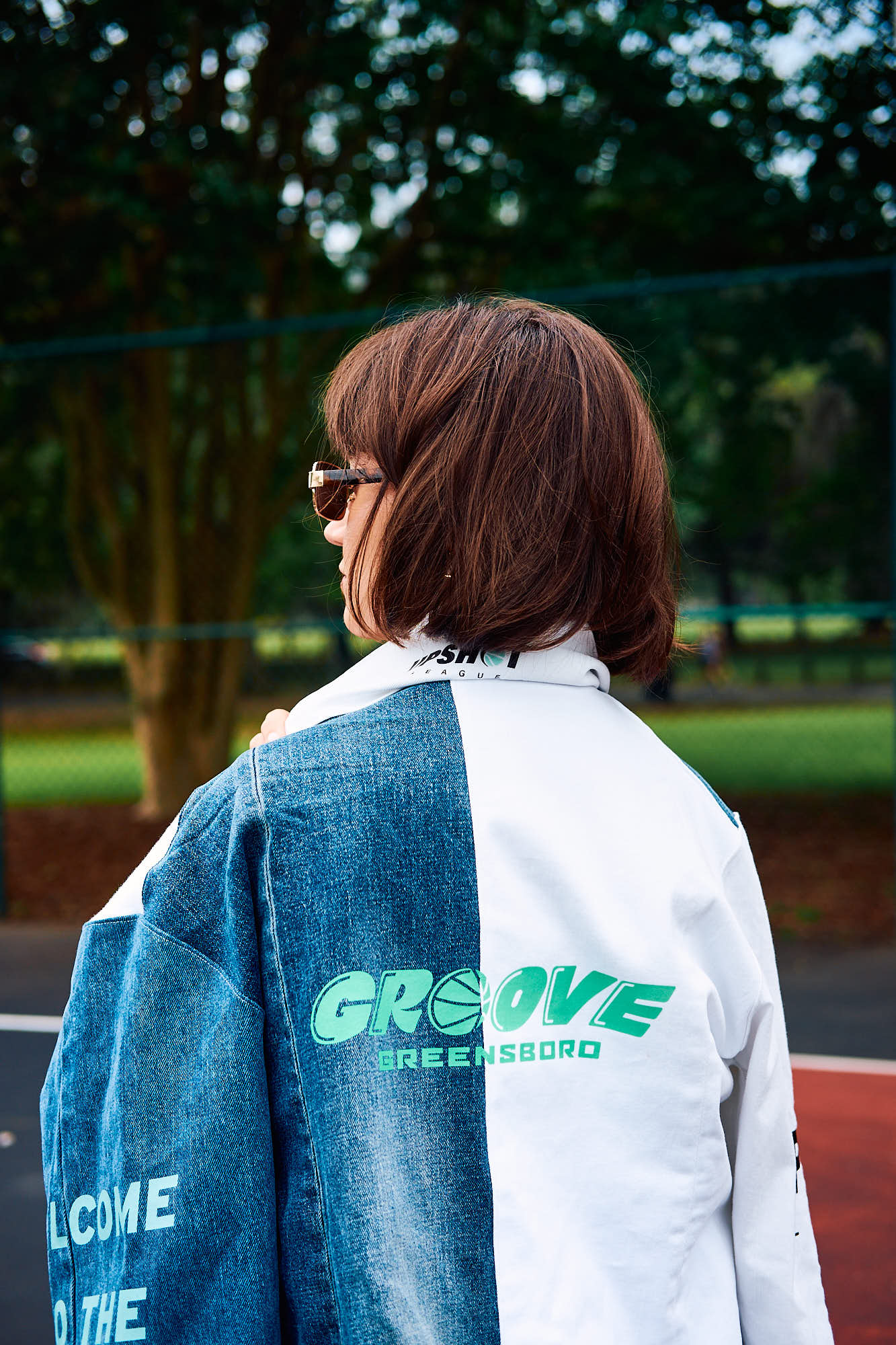 Person wearing a denim blue and white jacket with 'GROOVE Greensboro' branding on a basketball court.