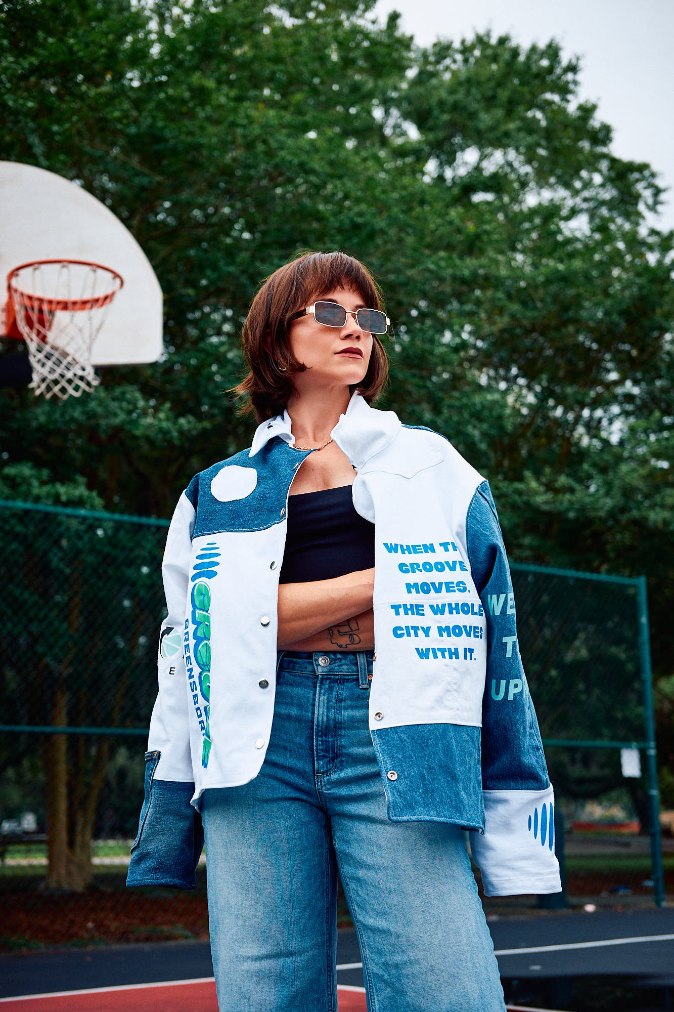 Person wearing a white and blue jacket with text and Greensboro Groove  branding, standing on a basketball court.