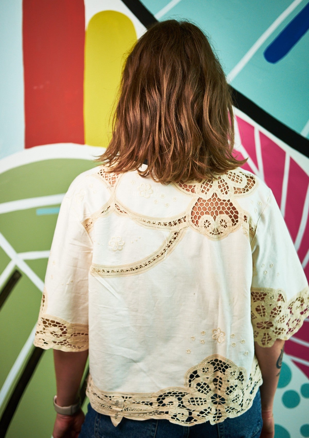 Person wearing a white blouse with lace details upcycled from a tablecloth in front of a colorful abstract painting