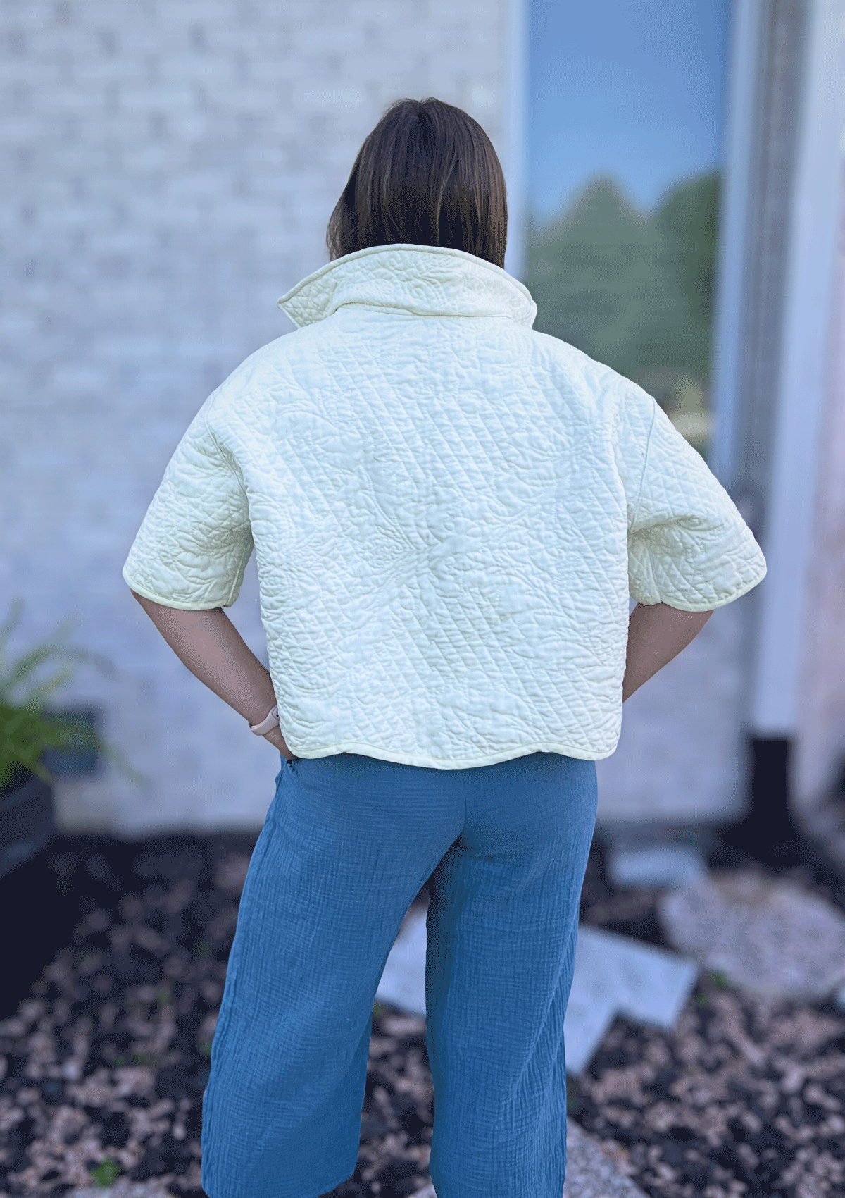 Person wearing a white jacket upcycled from a quilt and blue pants standing outdoors.