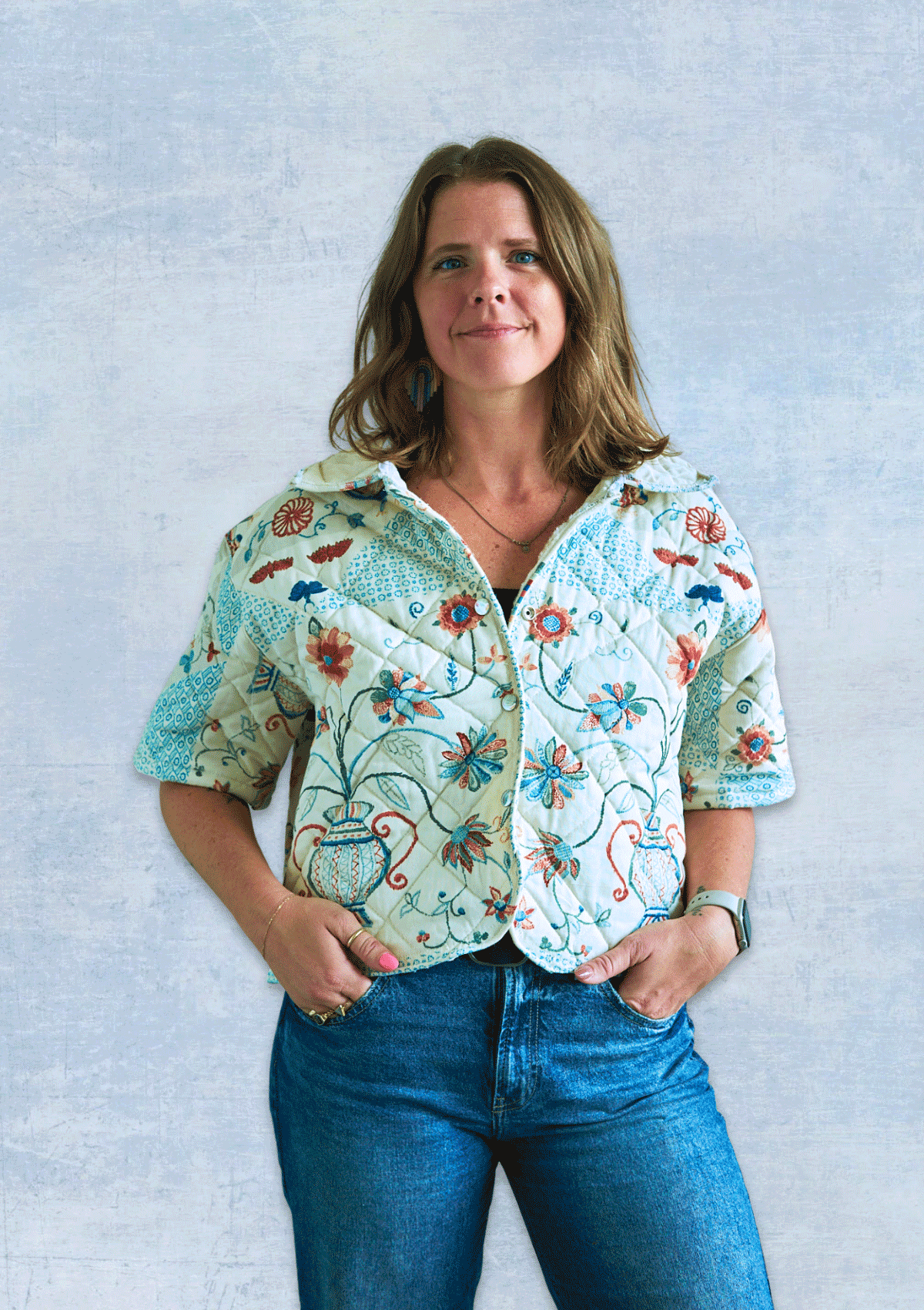 Woman wearing a jacket made from an upcycled quilt against a light blue background