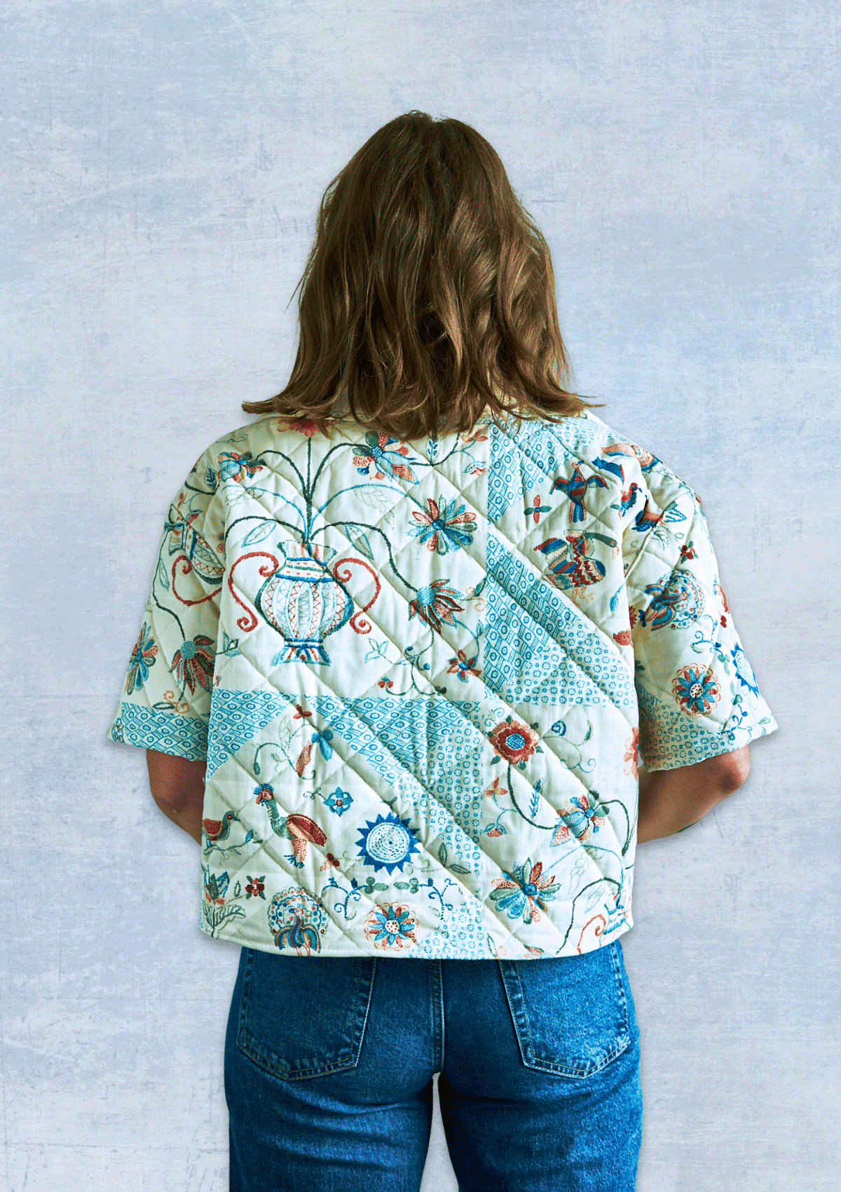 Person wearing a jacket made from an upcycled floral quilt against a light gray background