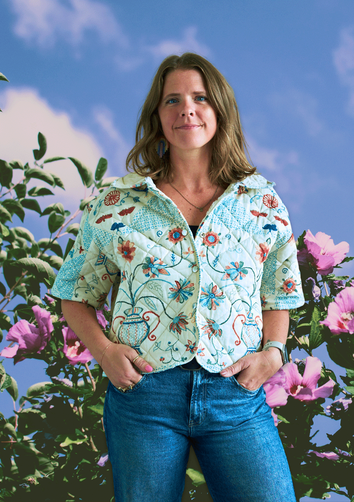 Woman wearing an upcycled floral jacket made from an upcycled quilt with a colorful background of flowers and sky.