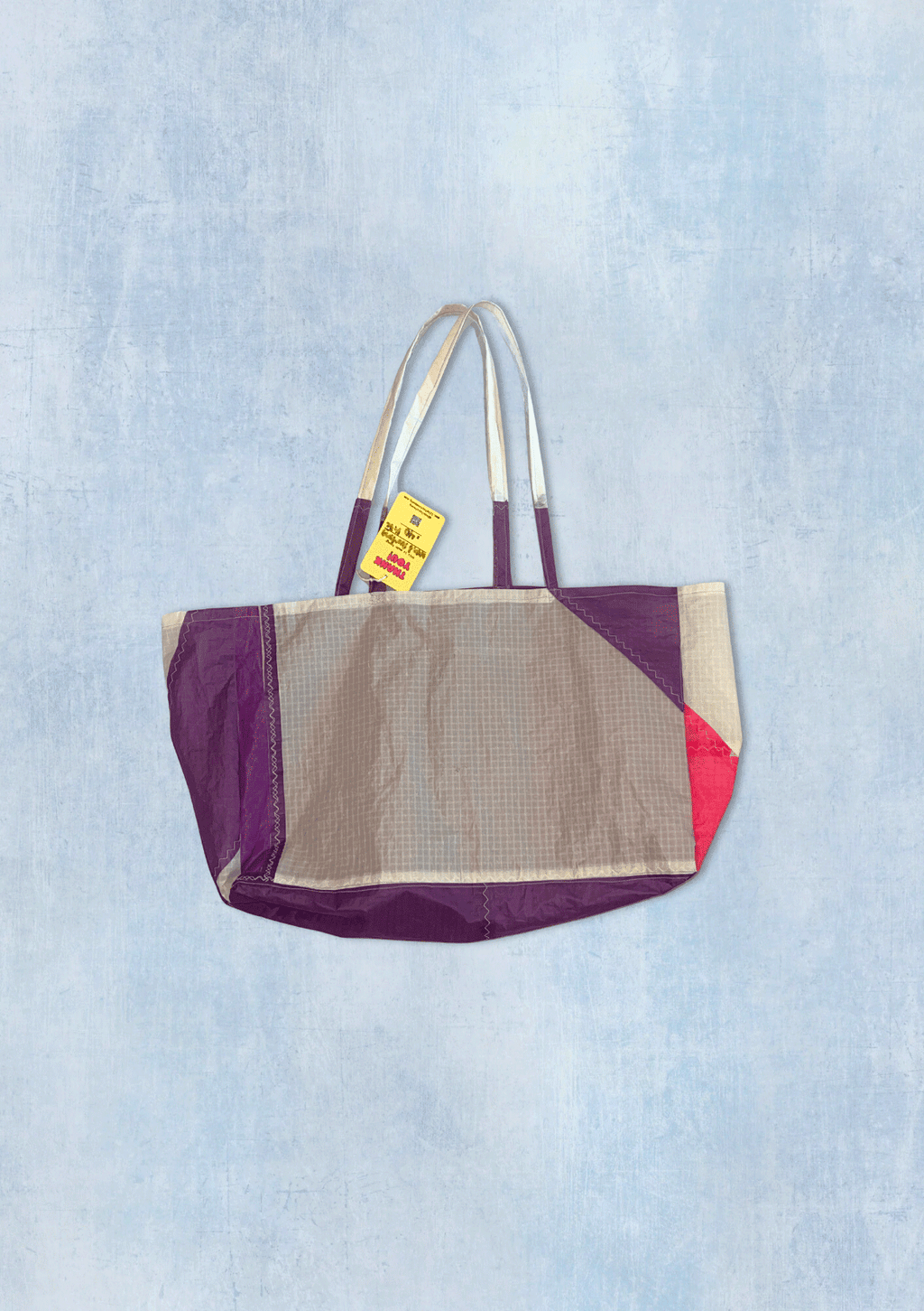 Multicolored tote bag upcycled from a windsurfing kite with a visible brand tag on a light blue denim background