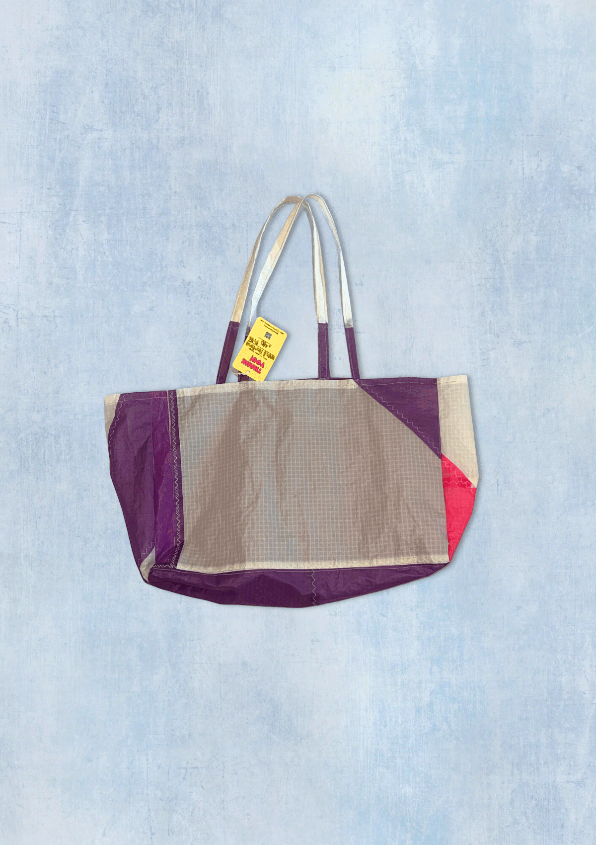 Multicolored tote bag upcycled from a windsurfing kite with a visible brand tag on a light blue denim background